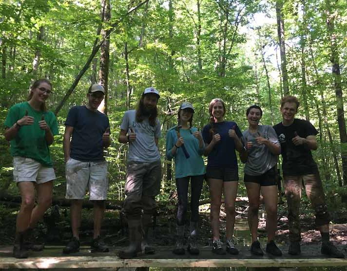 7 sustainability people- staff and students- stand lined up on a boardwalk 的y just repaired with thumbs up
